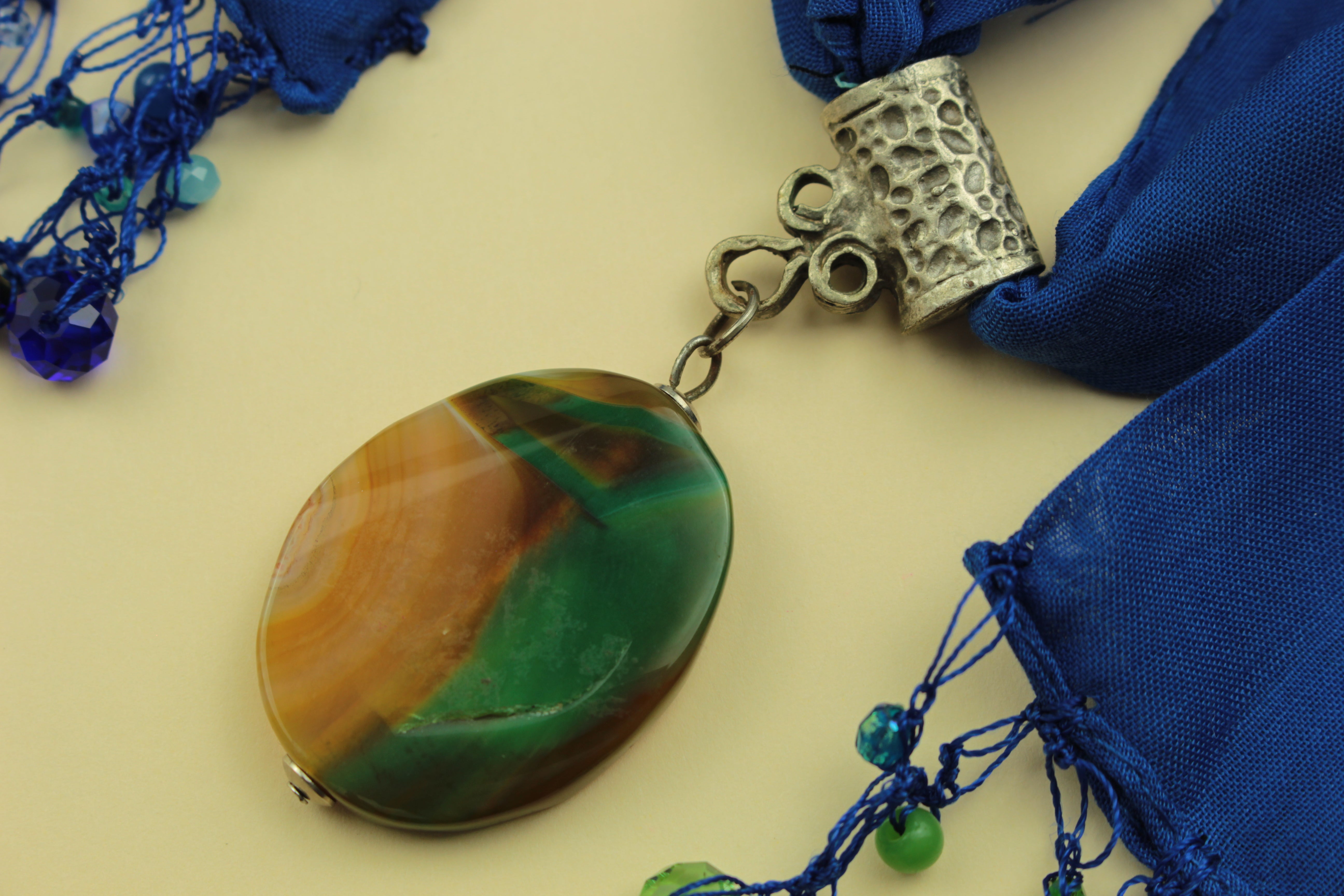 Blue scarf necklace with a natural stone pendant on a warm cream background, handmade in Tauranga