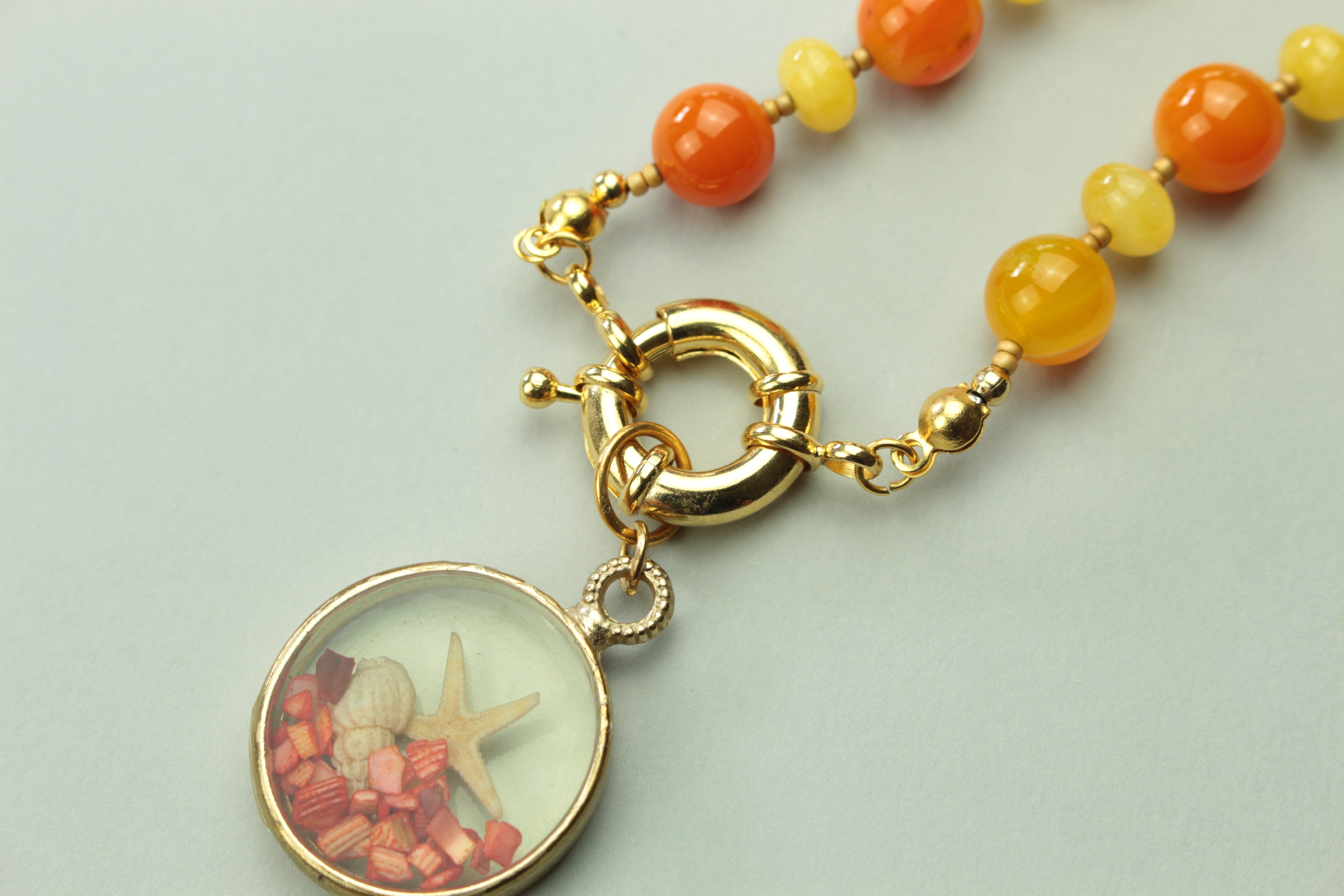 Golden summer seashell pendant necklace on a warm cream background, handmade in Tauranga